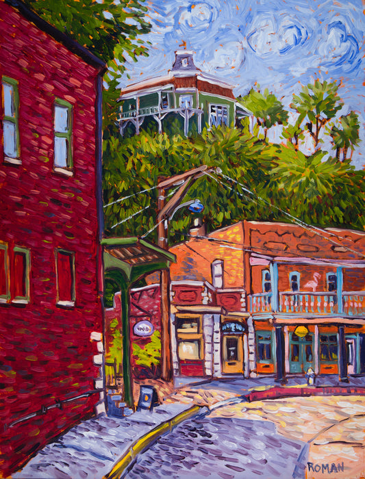 Impressionistic oil painting of a curving street in Eureka Springs, with a red brick building on the left, orange brick shops with a blue balcony and pink flamingo across the street, and a green Victorian house on a wooded hill under a swirling blue sky.